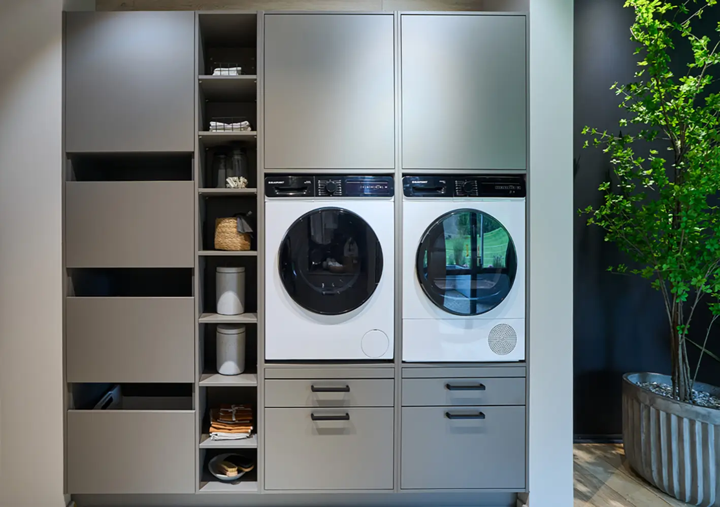 Meuble de buanderie gris avec lave-linge et sèche-linge intégrés et colonnes de rangement.
